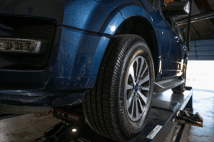 Colorado’s traction law, auto repair in Englewood, CO by Autovisions. A blue vehicle on a lift with a focus on its tires, ensuring accurate alignment for optimal driving performance and safety.