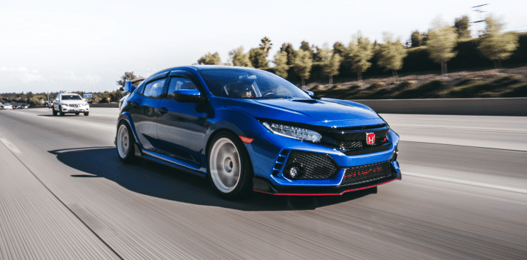 A vibrant blue Honda Civic Type R speeds down a multi-lane highway surrounded by trees and other vehicles. The sporty car, known for its distinctive aggressive front bumper and sleek design, exemplifies the excellence often celebrated in Japanese auto repair.