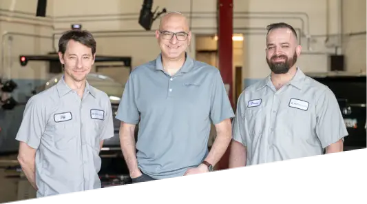 Auto repair in Englewood, CO at Autovisions. Image of Nathan Bryant and his 2 colleagues standing inside the shop, wearing uniforms, showcasing professionalism and dedication to quality auto repair services.