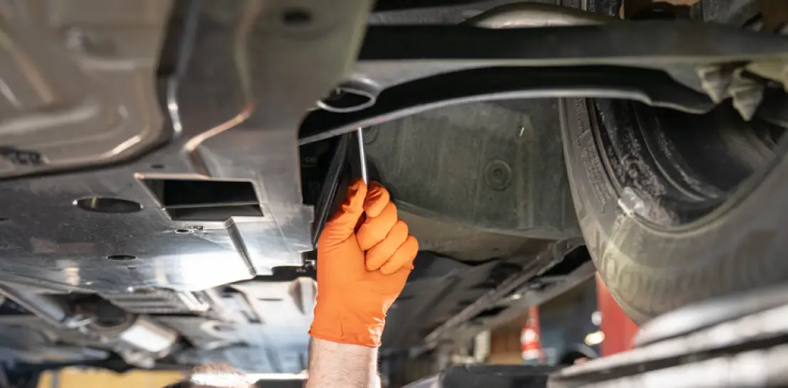Suspension repair in Englewood, CO by Autovisions. Image of a mechanic’s gloved hand tightening a bolt underneath a vehicle, showcasing professional suspension service for safety and performance.