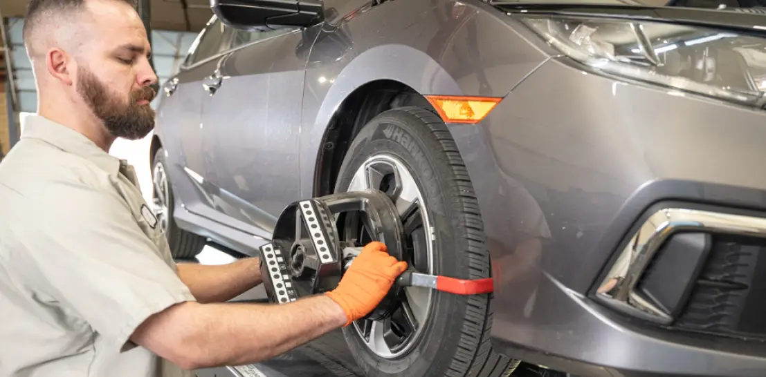 Wheel Alignment Service in Englewood, CO by Autovisions. Image of a technician performing a wheel alignment on a gray sedan using advanced alignment equipment, ensuring precision, safety, and improved vehicle handling.